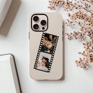 May include: A beige phone case featuring a film strip design. The film strip displays two photographs. The phone case has a camera module with three lenses. The background is white with dried flowers.