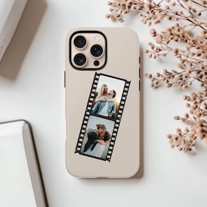 May include: A beige phone case with a black camera module and a film strip design. The film strip features two photographs of couples. The case is on a white surface with a book and dried flowers in the background.