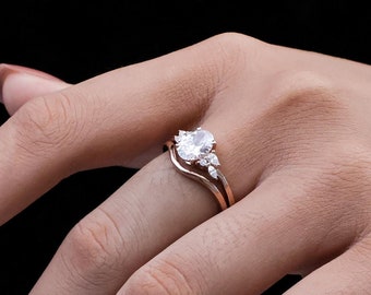 May include: A rose gold engagement ring set with a large round center stone and smaller accent stones. The ring is worn on the finger of a hand.