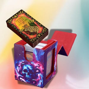 May include: A Universal Waite Tarot Deck with a decorative box. The deck has a red, gold, and black design. The box is purple with a skull and cosmic design. The box is open, revealing the cards inside.