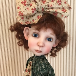 May include: A porcelain doll with red curly hair wearing a green plaid dress with a floral print bodice and a floral print bow.