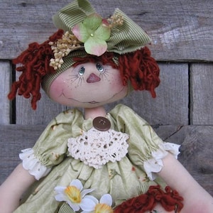 May include: A handmade rag doll with red yarn hair, a green and white striped hat, and a green and white floral dress. The doll is holding a smaller doll with red yarn hair.