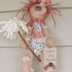May include: A rag doll with red yarn hair, wearing a pink and white dress with a heart that says "Hang It". The doll is holding a white yarn mop and a tag that says "I Had A Very Bad Day!"