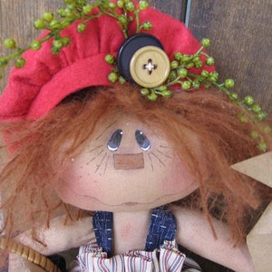 May include: A handmade rag doll with red hair, wearing a red felt hat with green sprigs and a black button. The doll is holding a brown paper windmill.