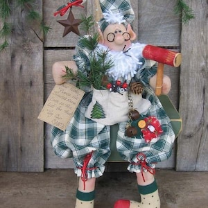 May include: A handmade Christmas elf doll wearing a green and white plaid outfit, a red and white hat, and red and white socks. The elf is holding a wooden mallet and a small bag with a pine tree, pine cones, and bells. The elf is sitting on a wooden bench with a sign that reads "Dear Elma... Please add Jennté's name back on the list for hat Toy Car SANTA".
