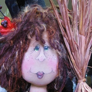 Könnte beinhalten: Eine handgemachte Stoffpuppe mit braunen Locken, die einen schwarzen Hut und ein braunes und schwarzes kariertes Kleid trägt. Die Puppe hält einen braunen Besen.
