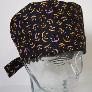Può includere: Un cappello da lavoro nero con una stampa a tema Halloween di zucche arancioni e viola su uno sfondo nero.