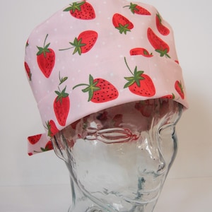 May include: A pink surgical scrub hat with a white polka dot pattern and a red strawberry print.