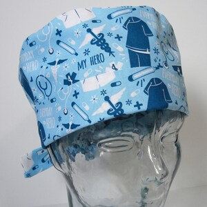 May include: A blue and white patterned surgical scrub hat with the text "Everyday Hero" and "My Hero" repeated throughout the design. The hat has a tie on the side.