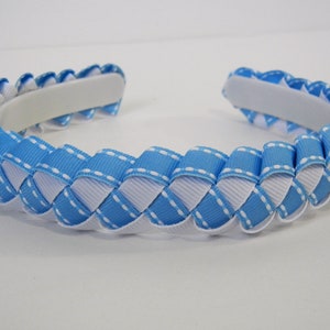 May include: A woven headband featuring alternating light blue and white ribbons. The ribbons are stitched together with white thread, creating a textured pattern. The headband has a white padded interior for comfort.