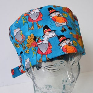 Pode incluir: Um gorro cirúrgico azul com um padrão de gnomos usando chapéus de peregrino e segurando abóboras e folhas de outono.