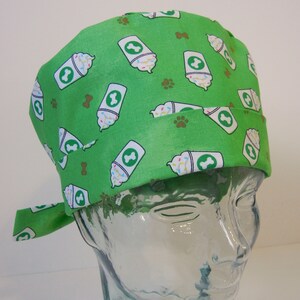 Op de afbeelding: Groene chirurgische scrub-muts met een patroon van witte en bruine ijsbekers met sprankels en poot afdrukken.