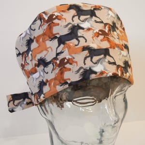 May include: A surgical scrub hat with a brown, white, and black horse print. The hat has a tie on the side.