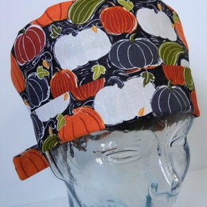 May include: A black scrub hat with a pumpkin and gourd print in orange, white, and green. The hat has a tie on the side.