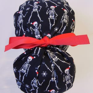 May include: A navy blue fabric item patterned with white skeletons in Santa hats and snowflakes. It's tied with a bright red ribbon, forming a bow. The design suggests a festive, holiday-themed product, suitable for gifting.
