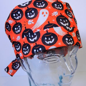 Puede incluir:  gorro de quirófano naranja y negro con un estampado de Halloween de calabazas y fantasmas.