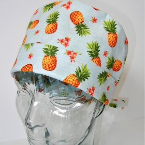 May include: A light blue surgical scrub hat with a pineapple print. The hat has a tie at the back.