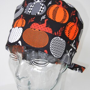 Può includere: Cappello da lavoro nero con stampa a zucca in arancione, bianco e grigio. Il cappello ha una cravatta sul retro.