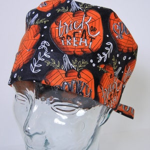 Può includere: Cappello da lavoro nero con una stampa di zucca arancione e nera. La stampa include il testo "trick or treat" e "spooky".
