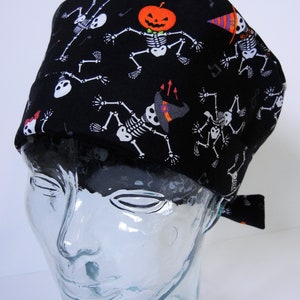 Può includere: Cappello da lavoro nero a tema Halloween con scheletri danzanti, una zucca e note musicali.