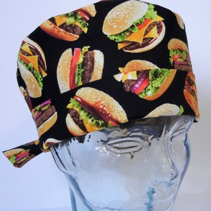 May include: A black scrub hat with a repeating pattern of colorful hamburgers. The hat has a tie that can be tied at the back of the neck.