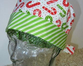 May include: A white and green striped scrub hat with a red and white candy cane pattern. The hat is made of fabric and has a tie at the back.