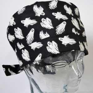 Può includere: Un cappello da lavoro nero con un motivo di fantasmi bianchi. Il cappello ha un laccio sul retro.