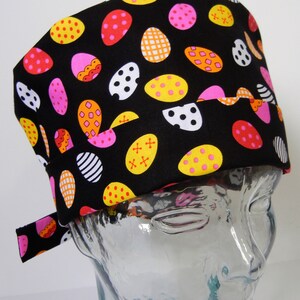 May include: Black scrub hat with a colourful Easter egg pattern. The hat has a tie that can be tied at the back of the neck.