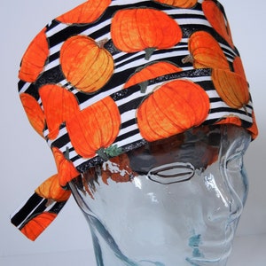Può includere: Un cappello da lavoro a strisce bianche e nere con un motivo di zucche arancioni. Il cappello ha una cravatta che può essere legata dietro la testa.