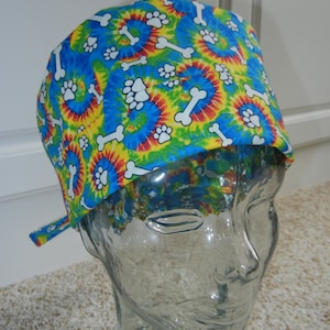 Op de afbeelding: Een blauwe, gele en rode tie-dye chirurgische scrub-muts met een wit poot- en botpatroon.