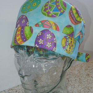 Könnte beinhalten: Eine blaue OP-Mütze mit einem bunten Osterei-Muster. Die Mütze hat einen Band hinten.