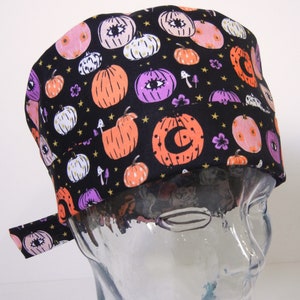 Pode incluir: Boné de trabalho preto com estampa de Halloween de abóbora e olho. O boné tem uma gravata lateral.