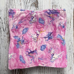 Puede incluir: Acogedor de cuenco de tela rosa con un estampado de unicornios. El acogedor presenta un diseño acolchado con un patrón repetido de unicornios blancos, nubes azules y acentos morados. El acogedor está diseñado para sostener un cuenco de comida caliente.