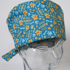 May include: A blue and yellow patterned surgical scrub hat with the text "Zero Barks Given" repeated throughout. The hat has a tie on the back.
