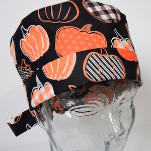 Può includere: Cappello da lavoro nero con stampa a zucca arancione e bianca. Il cappello ha una cravatta sul retro.