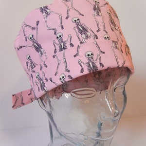 Puede incluir: Un gorro quirúrgico rosa con un patrón repetido de esqueletos negros.