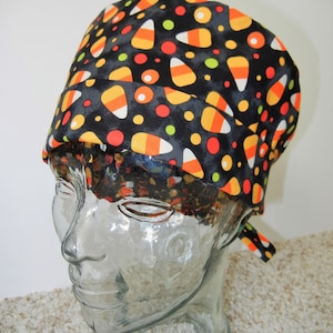 Può includere: Un cappello da lavoro nero con un motivo di mais dolce di Halloween e pois. Il cappello ha una cravatta sul lato.