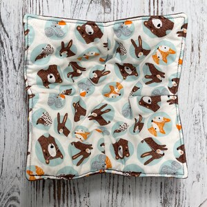 Könnte beinhalten: Ein quadratischer, gesteppter Schalenwärmer mit einem skurrilen Waldtiermuster. Der Stoff zeigt braune Bären, Füchse und Kaninchen in hellblauen Kreisen auf cremefarbenem Hintergrund. Der Wärmer ist so konzipiert, dass er eine Schüssel hält und die Hände vor Hitze schützt.