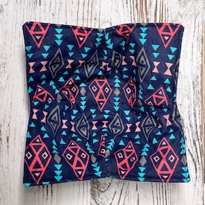 Könnte beinhalten: Ein marineblauer Schüsselwärmer mit einem geometrischen Muster aus roten, türkisfarbenen und grauen Formen. Das Design umfasst Diamanten, Dreiecke und andere Formen. Der Wärmer ist quadratisch und scheint aus Stoff zu sein.