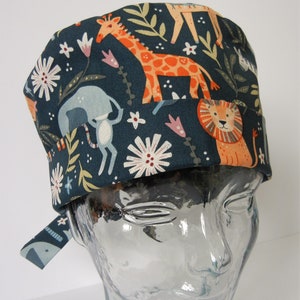Può includere: Un cappello da lavoro blu scuro con una stampa colorata di animali e fiori. Gli animali includono una giraffa, un leone e un elefante. I fiori sono bianchi, rosa e gialli.