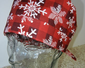 May include: Red and white patterned scrub hat with a red and black plaid design and white snowflakes. The hat is on a glass head form.