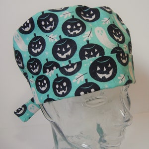 Pode incluir: Um gorro de cirurgia azul turquesa com uma estampa de Halloween em preto e branco de abóboras e fantasmas.