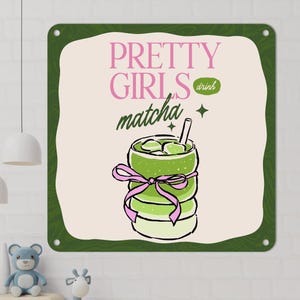 May include: A square metal sign with a green border and the words "PRETTY GIRLS matcha drink" in pink and green. The sign features a matcha drink illustration with a pink bow.
