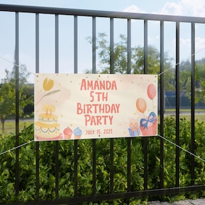 Może przedstawiać: Kremowy baner na 5. urodziny Amandy, z ciastem, babeczkami, balonami i prezentami. Na banerze widnieje napis "Amanda 5th Birthday Party July 15, 2025" w kolorze czerwonym i pomarańczowym.