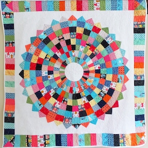 May include: A colorful handmade quilt with a central circular design. The quilt features a white background with a large, vibrant circle composed of various fabric squares in shades of red, blue, green, and orange. The border is a mix of patterned fabrics.