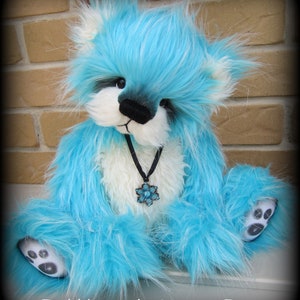 May include: A blue and white teddy bear with a black necklace and a blue flower charm. The bear has a fluffy, long-haired coat.