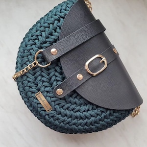 May include: Teal crochet handbag with a black leather flap, gold buckle and rivets. The bag has a gold chain strap and a small gold tag reading "zaplatana".