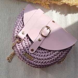May include: A light pink crocheted handbag with a leather flap and a gold buckle. The bag has a gold chain strap and a small gold tag with the text "zaplat.ana" on it.