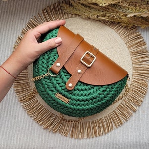 May include: A green crocheted bag with a brown leather flap and a gold buckle. The bag has a gold chain strap and a small leather tag that says "zaplatana".