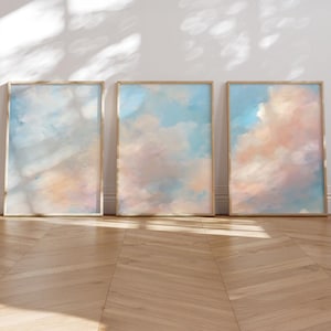 May include: Three vertical rectangular framed wall art pieces featuring abstract oil paintings of a sky with soft clouds in shades of light blue, pale pink, and white. Each piece is enclosed in a thin, light-colored wooden frame.